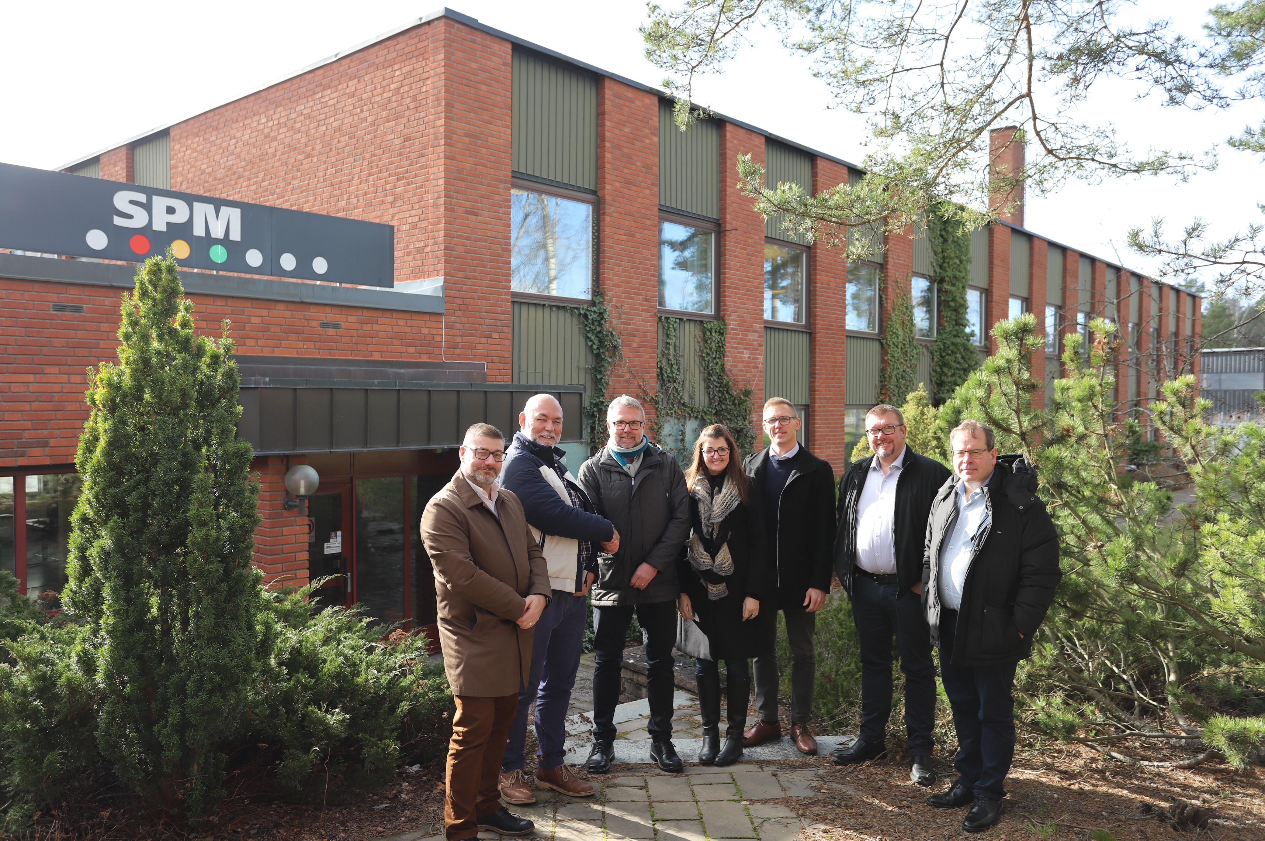 WearCheck and SPM Instrument representatives shaking hands in a sunny setting in front of SPM headquarters